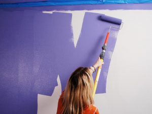 Woman painting purple wall with roller.